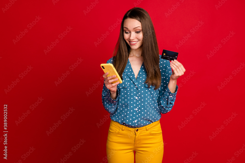 Portrait of attractive cheerful focused girl using device bank card paying service app isolated on bright red color background Portrait of attractive cheerful focused girl using device bank card paying service app isolated on bright red color background