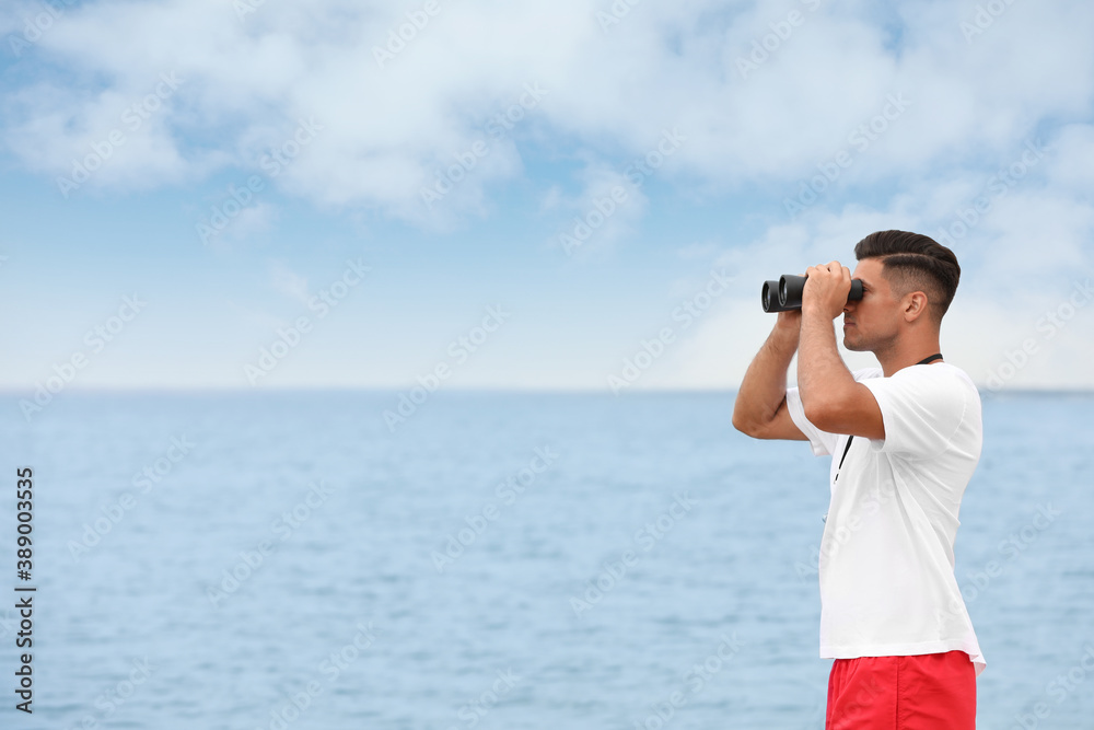 Obraz premium Handsome male lifeguard with binocular near sea