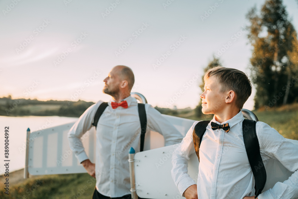 Father and son wearing jetpack wings posing in sunny parkland Father and son wearing jetpack wings posing in sunny parkland