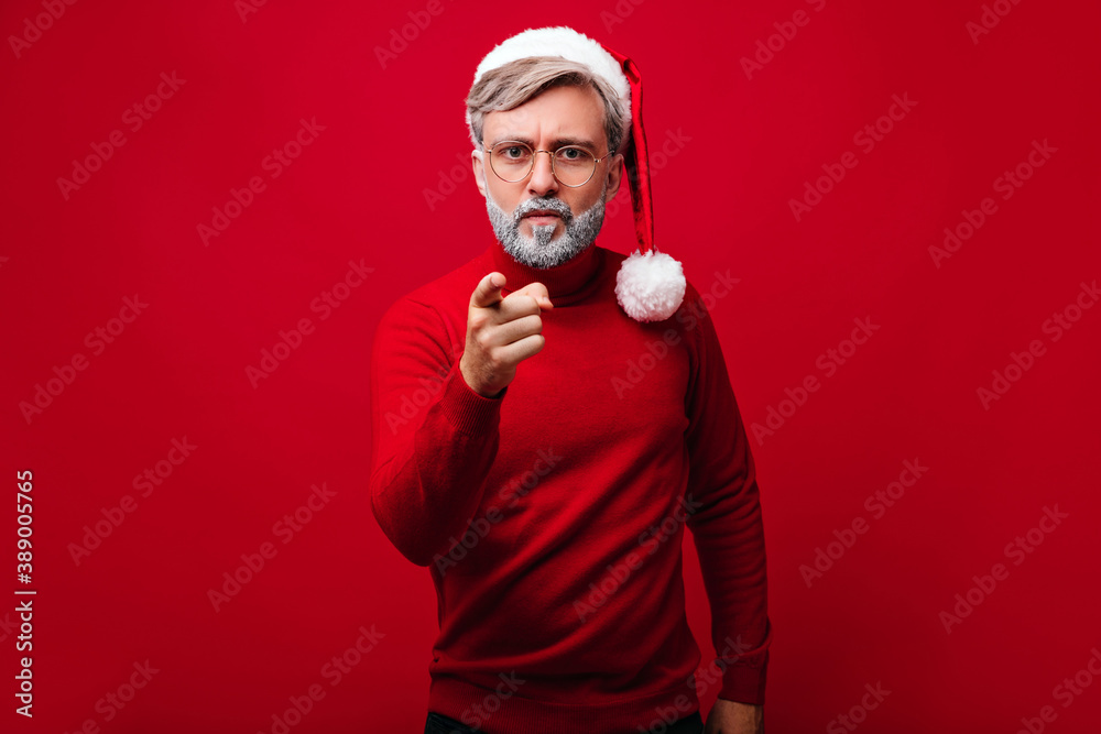 Funny old man in glasses wears santa claus hat during photoshoot. Handsome white-haired model preparing for new year. Funny old man in glasses wears santa claus hat during photoshoot. Handsome white-haired model preparing for new year.