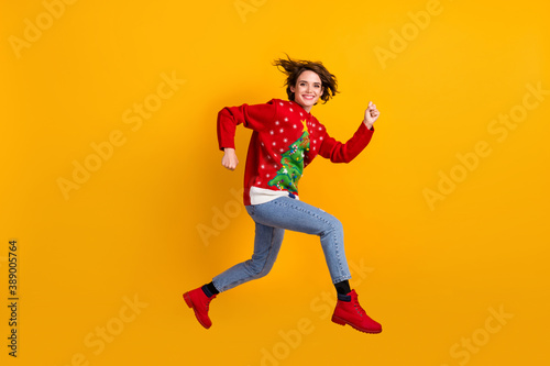 Full size profile side photo of cheerful girl jump run x-mas tradition discounts wear christmas tree theme decor sweater pullover denim jeans isolated bright shine color background