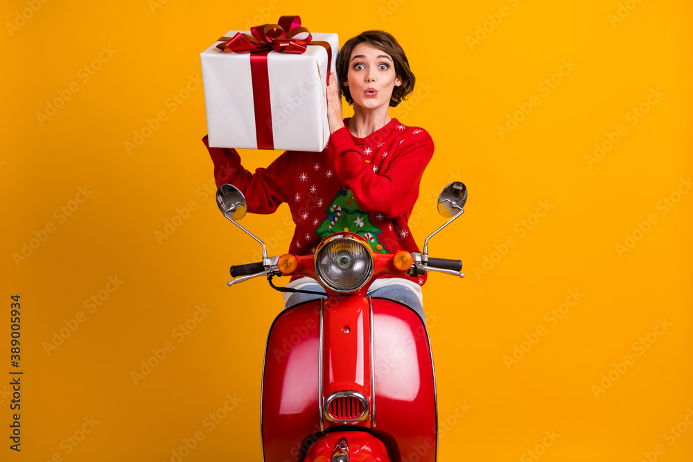 Fototapeta premium Photo of astonished girl in christmas tree ornament sweater pullover shake gift box drive red scooter x-mas eve noel party isolated over bright shine color background