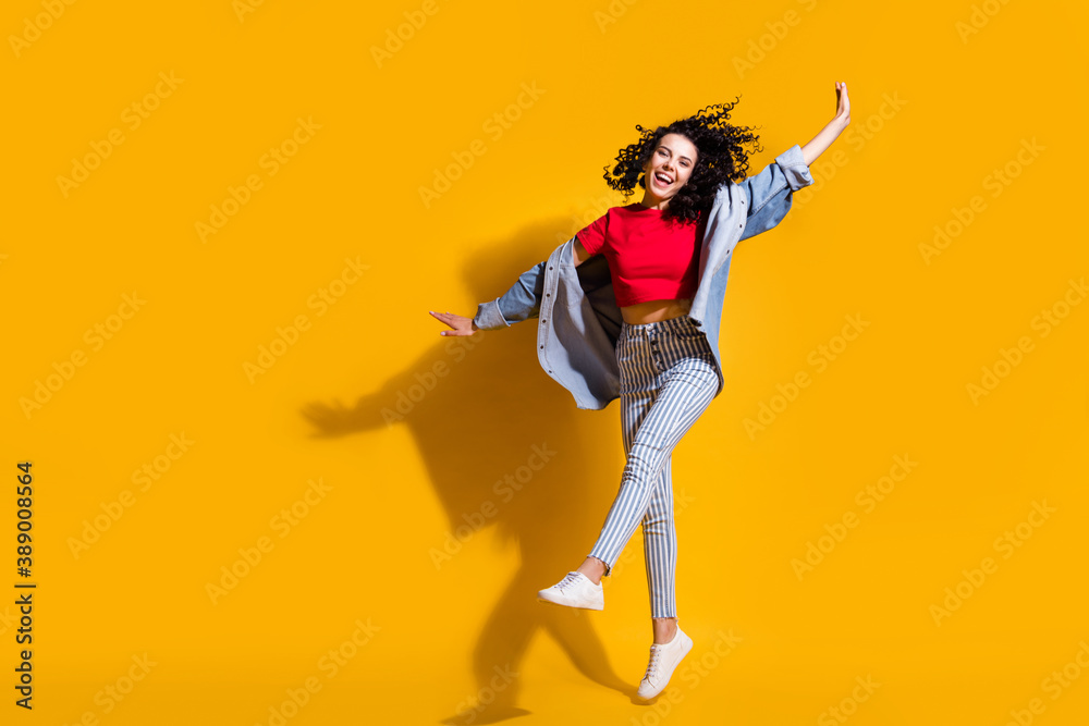 Full length photo of lady jump raise leg hands wear striped jeans cropped red t-shirt jacket sneakers isolated yellow color background
