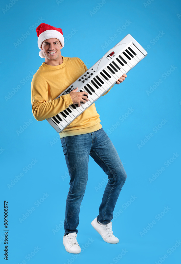 Man in Santa hat playing synthesizer on light blue background. Christmas music Man in Santa hat playing synthesizer on light blue background. Christmas music