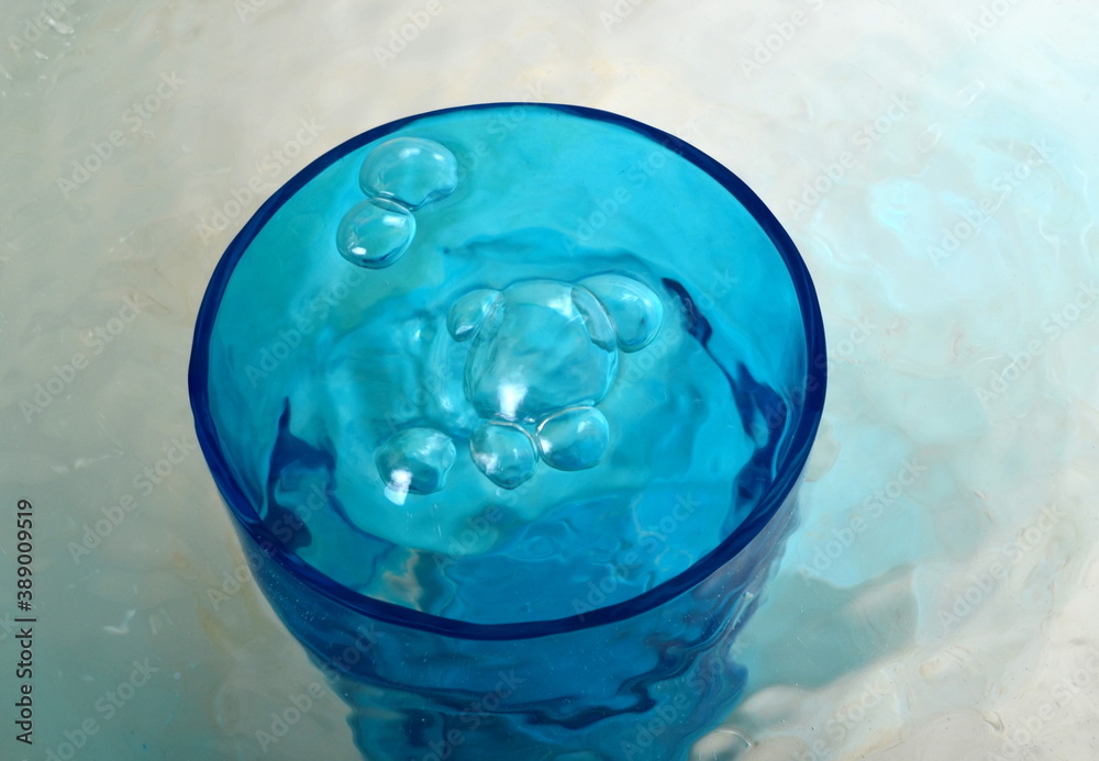 Overflowing water in a blue glass, full overflow glass with water and bubbles Overflowing water in a blue glass, full overflow glass with water and bubbles