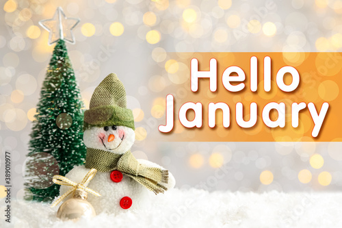 Greeting card with text Hello January. Little toy snowman and fir tree on snow against blurred Christmas lights