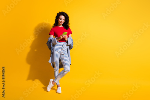 Photo of girl hold telephone look screen wear striped jeans red t-shirt jacket sneakers isolated yellow color background