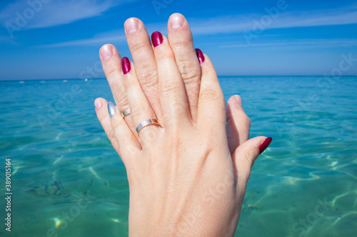 Holding Hands with wedding Rings on the sea Background. A romantic vacation, a love honeymoon.