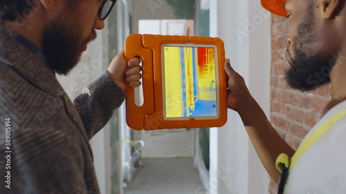 Back view of professional construction team using infrared camera on tablet checking heating system