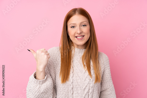 Young redhead woman over isolated pink background pointing to the side to present a product