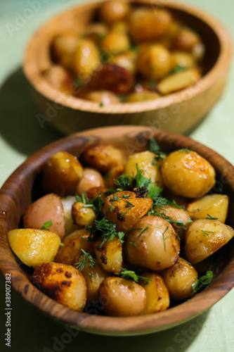two wooden plates with fried whole new potatoes close up seasoned with herbs
