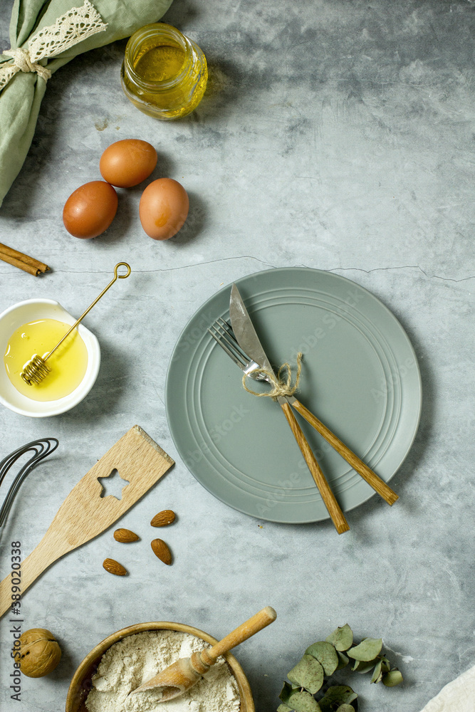 Ingredients for a baking recipe on a dark table eggs, flour, honey, nuts and an empty plate with cutlery, flat lay, copy space, top view Ingredients for a baking recipe on a dark table eggs, flour, honey, nuts and an empty plate with cutlery, flat lay, copy space, top view