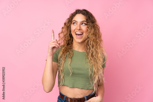 Young blonde woman with curly hair isolated on pink background intending to realizes the solution while lifting a finger up