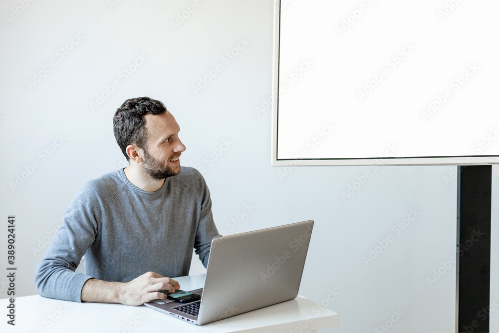 young man sits at laptop and shows presentation on tv