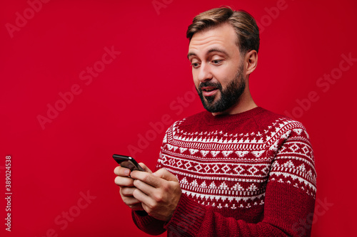 Interested man with beard texting message. Good-humoured guy in new year sweater looking at phone screen. © Look!