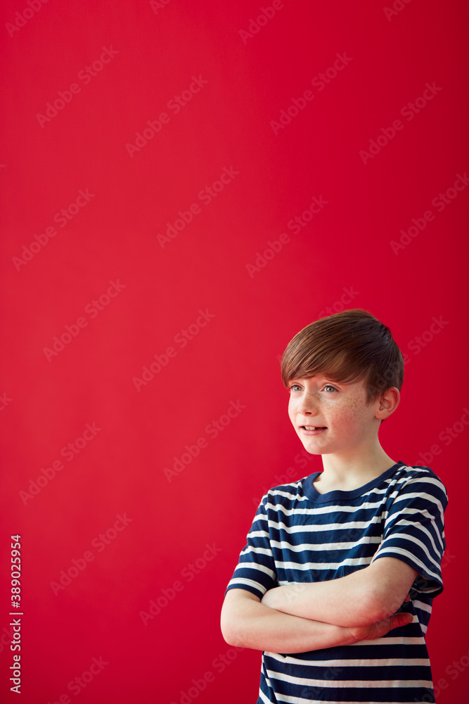 Portrait Of Young Boy With Folded Arms Against Red Studio Background Smiling At Camera Portrait Of Young Boy With Folded Arms Against Red Studio Background Smiling At Camera