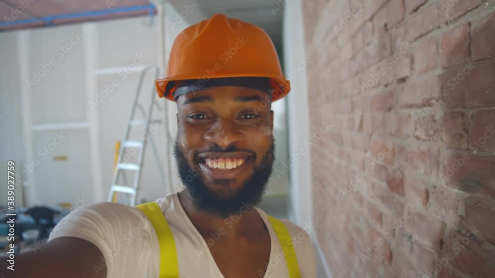 Pov shot of african builder in safety helmet taking selfie over construction site background
