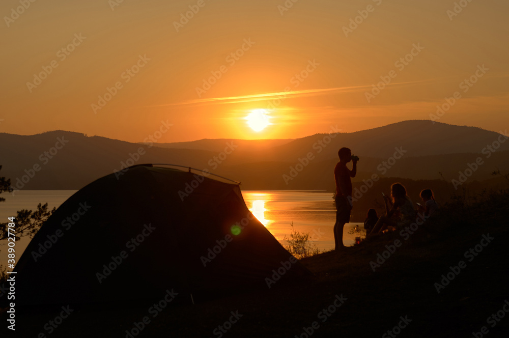 Silhouette group of people and touristic tent against sunset on the lake
