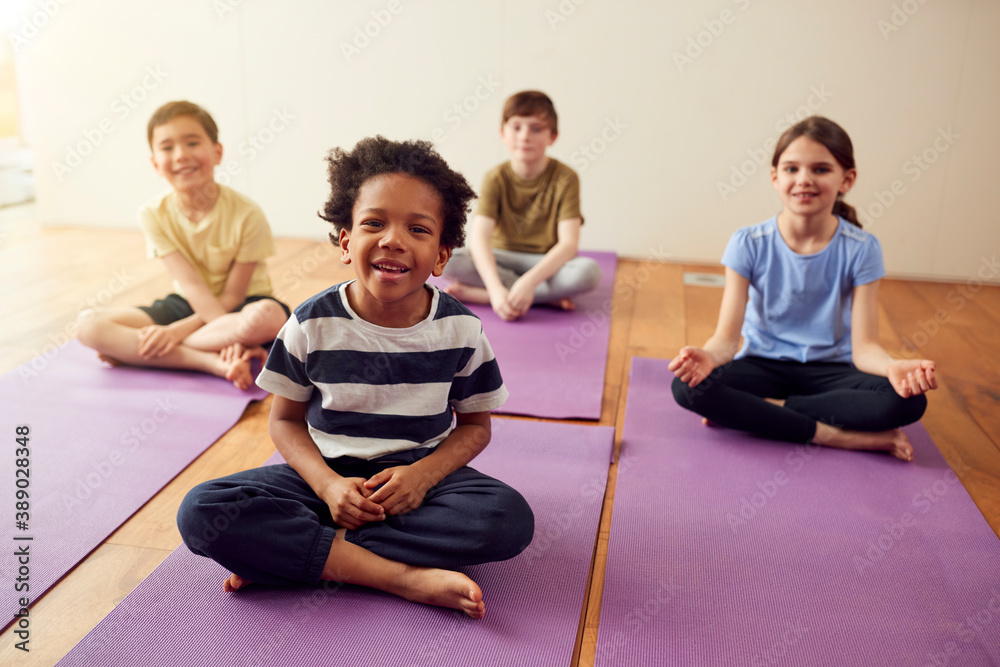Portrait Of Group Of Children Sitting On Exercise Mats In Exercise Class Portrait Of Group Of Children Sitting On Exercise Mats In Exercise Class