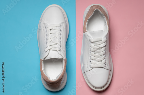 White leather sneakers on a blue and pink background. A pair of trendy white athletic shoes or sneakers with copy space. flat lay