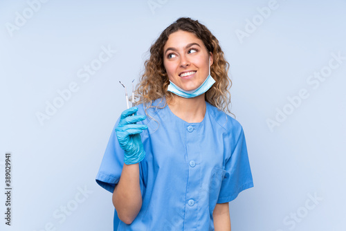 Young blonde woman dentist holding tools isolated on blue background laughing and looking up