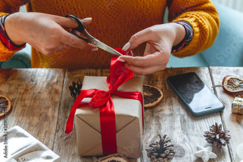 Young woman wrapping christmas present on table with new year deorations
