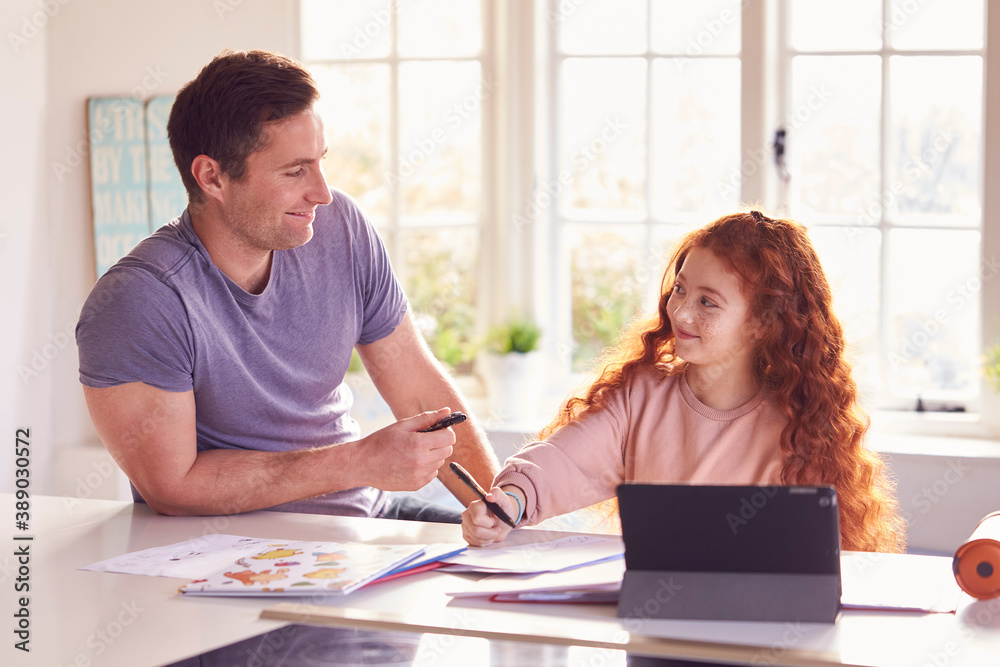 Fototapeta premium Father Helping Daughter With Homework Sitting At Kitchen Counter Using Digital Tablet Together