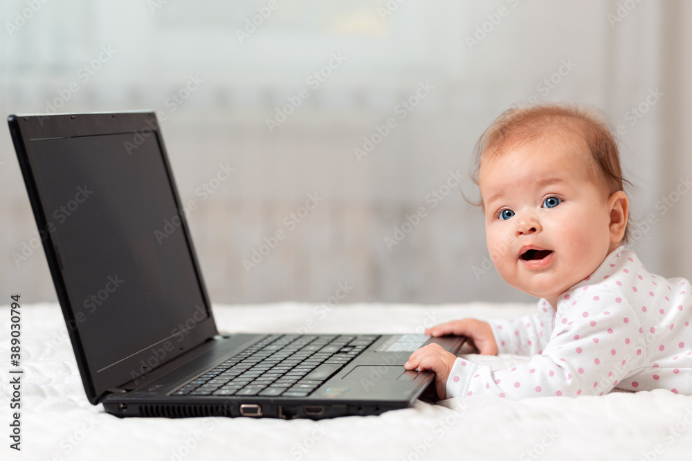 Happy baby is lying on the bed and holding on to the laptop with his hands. The concept of entertainment and education for children using the Internet