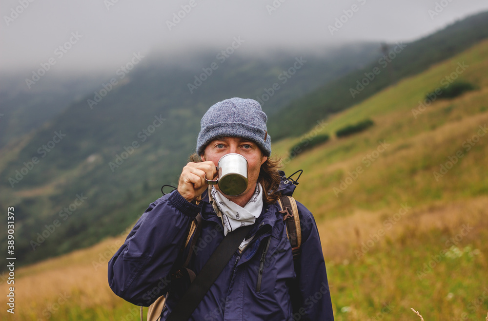 Hiker drinking hot drink from cup in mountains. Refreshment during hiking in cold weather