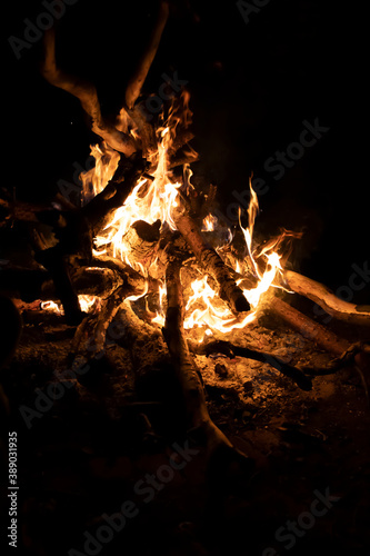 close-up of a campfire at night with orange flames and burning wood, smoke, fire and sparks on black background, front view