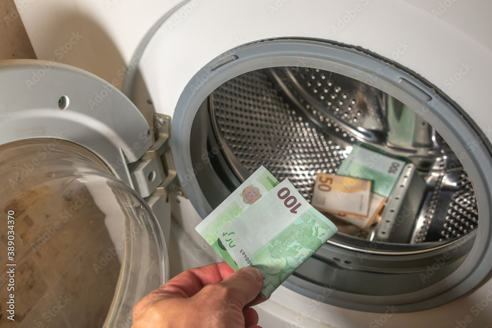 Money laundering concept, a man hand adding the 100 euro banknote into a pile of euro banknotes to be cleaned inside the washing machine, background, details.