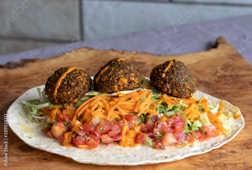 Wrap with falafal balls, colourful salad, with sauce over. photo