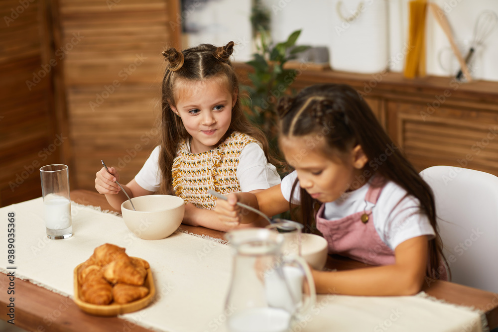 happy little children girls friends having breakfast - fresh delicious croissants and milk in the kitchen.