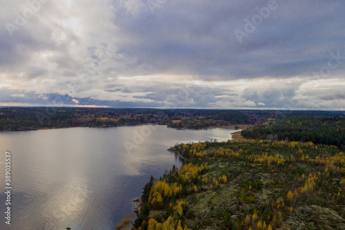 Rocky island with colorful autumn trees on Lake Ladoga and the sky reflected in the water