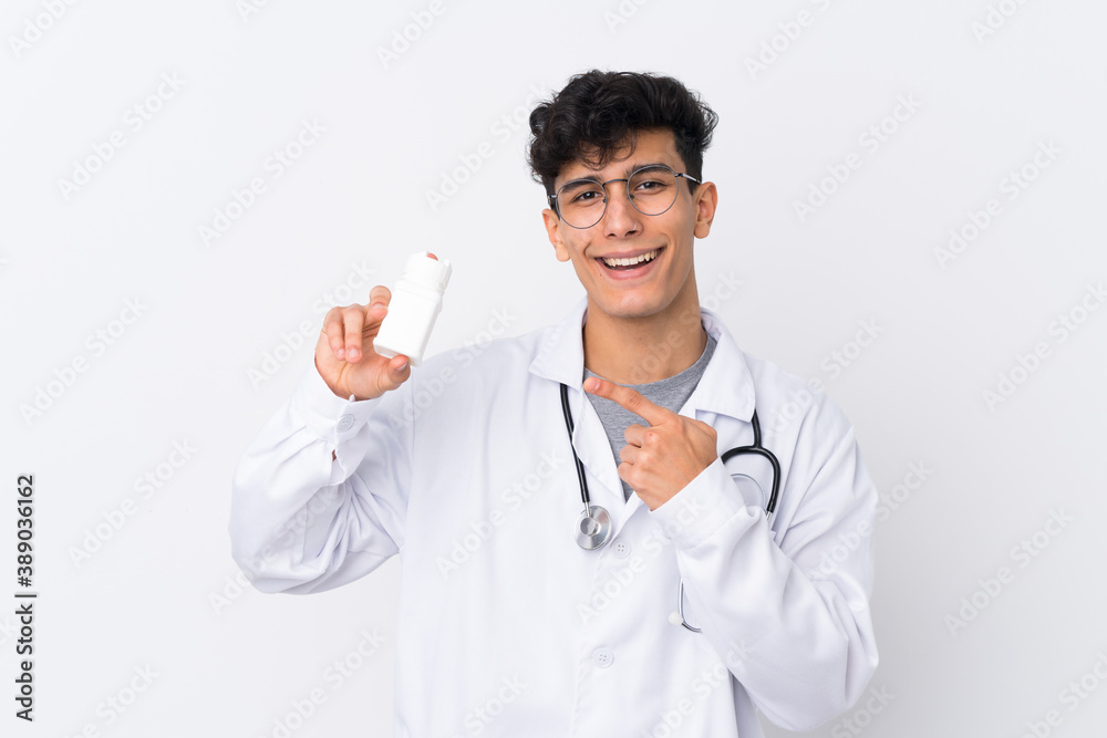 Young Argentinian man over isolated white background wearing a doctor gown and holding pills Young Argentinian man over isolated white background wearing a doctor gown and holding pills