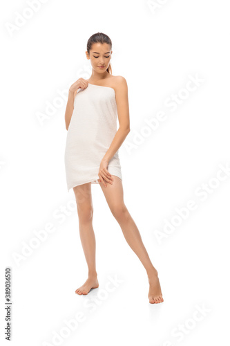 Beautiful woman looks at her legs isolated on white background. Beauty, cosmetics, spa, depilation, treatment and health concept. Fit and sportive, sensual body with well-kept skin in towel. Copyspace