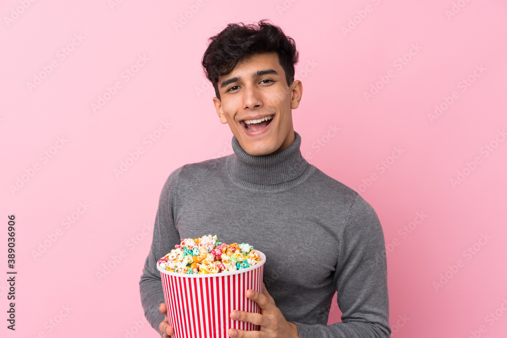 Young Argentinian man over isolated white background holding a big bucket of popcorns Young Argentinian man over isolated white background holding a big bucket of popcorns