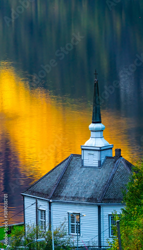 Small white chapel by a fjord with calm water  reflecting the yellow light from the sunset.