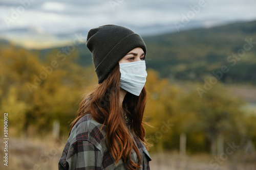 Traveler with a medical mask on her face and a hat in the autumn forest