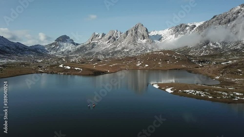 Aerial view of a high mountain landscape with snow and a lake where there are people paddle surfing