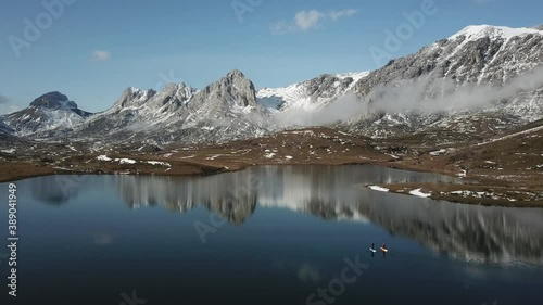 Aerial view of a high mountain landscape with snow and a lake where there are people paddle surfing