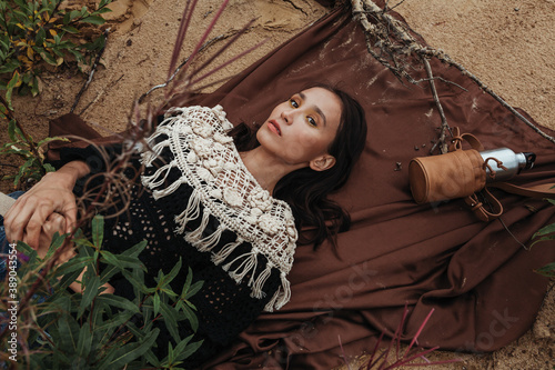 фотографія Stylish and pretty asian woman-traveller lying on a brown plaid on the sand