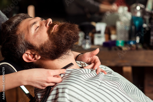 Barber shaving a bearded man, close-up. Beard styling and cut. Vintage barber shop. Long beard.