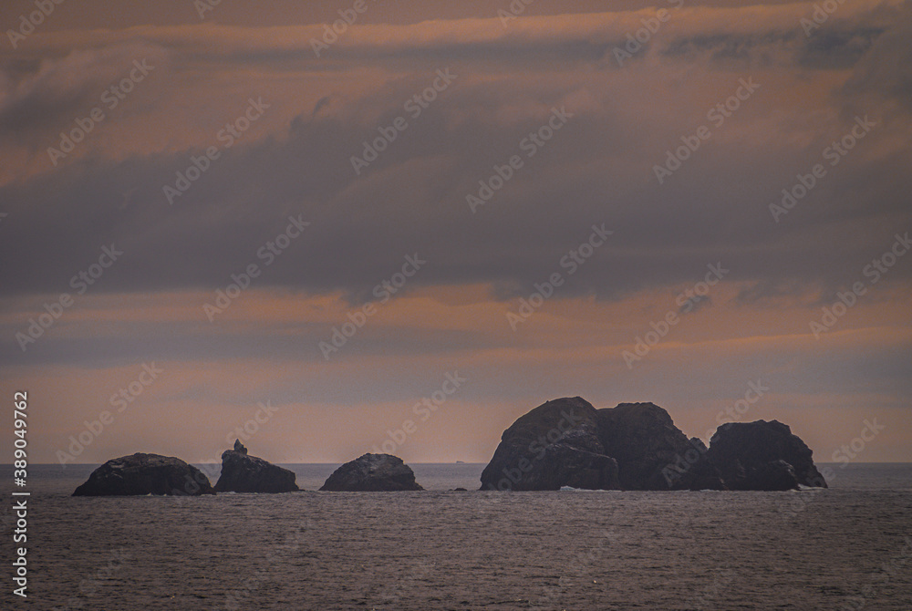 Cape Horn, Wollaston Islands, Chile - December 14, 2008: Rocks stick above dark gray water under early morning orange and blueish cloudscape.