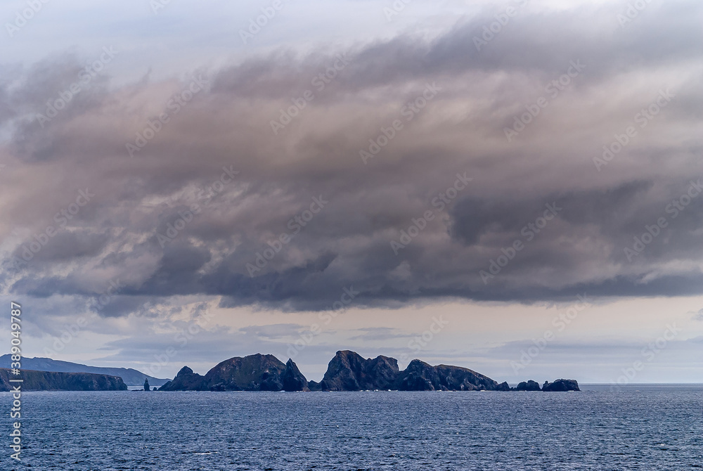 Cape Horn, Wollaston Islands, Chile - December 14, 2008: Black rocks peak out of blue ocean at edge of archipelago under brownish cloudscape.