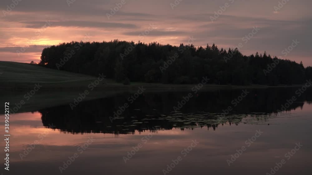 Sunset at the forest lake. A background of the peaceful panoramic landscape of the evening at the lake-shore in the summer end to autumn season. Scenic sunlight in cloudy sky above a woods. Sunset at the forest lake. A background of the peaceful panoramic landscape of the evening at the lake-shore in the summer end to autumn season. Scenic sunlight in cloudy sky above a woods.