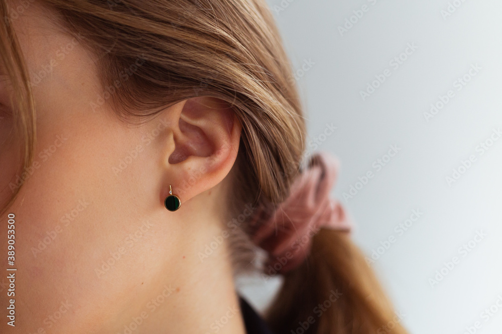 Obraz premium Golden earring with green stone against hair tied up in a ponytail