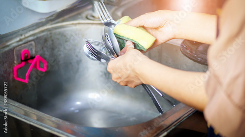 Woman washing spoons and forks in the kitchen close-up