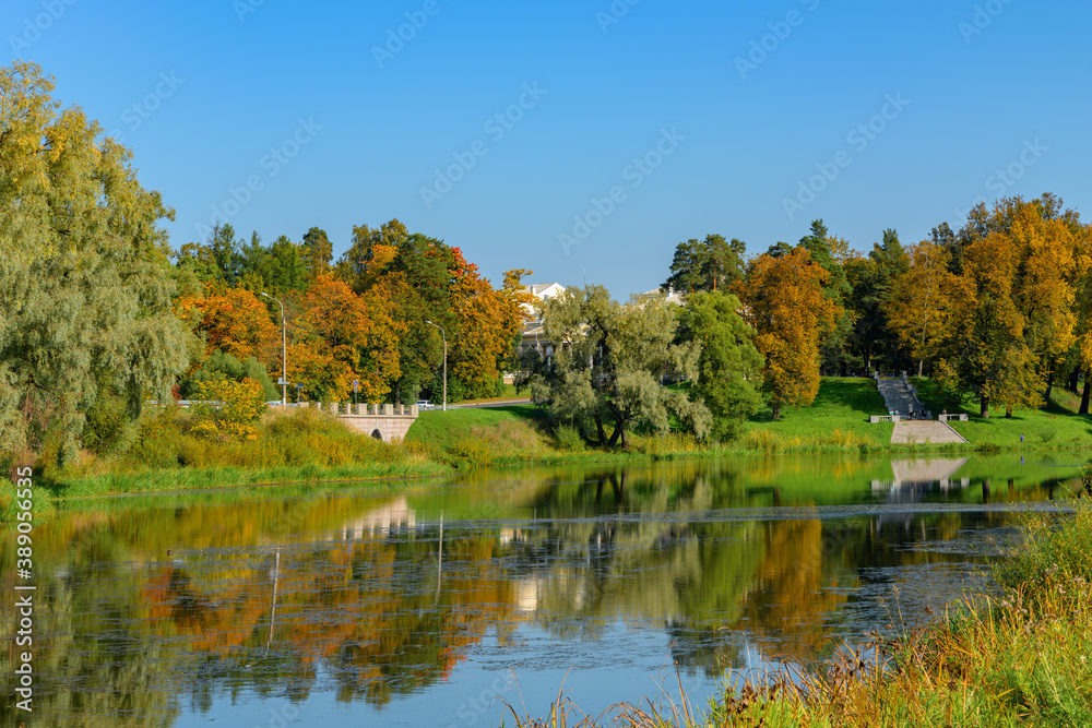 Bright colorful autumn landscape, trees near river and blue sky, Bolshoy Kamenny bridge-dam and Mariental Staircase, which connects the pond to the site opposite the Imperial Palace in Pavlovsk