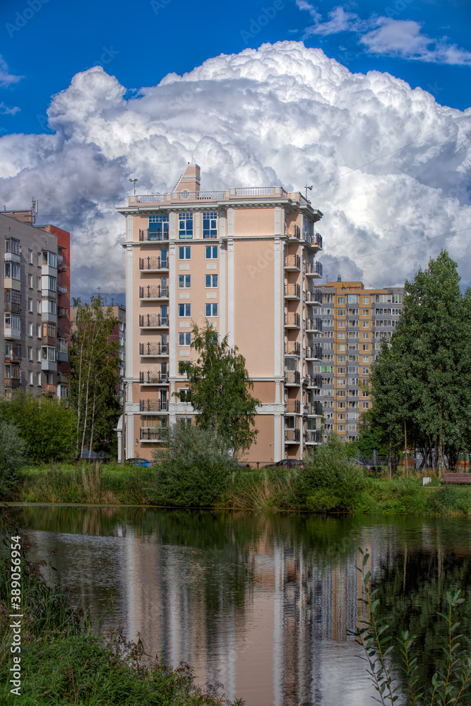 Public city park with pond and reeds and multi-storey dwelling buildings behind under blue sky with amazing clouds at sunny autumn day